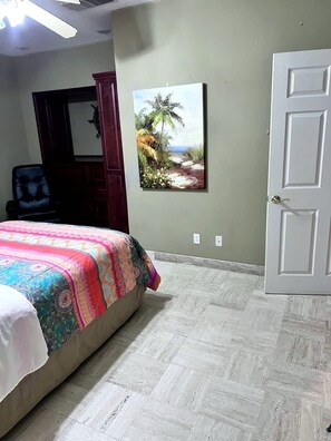 A bedroom with a bed, a door, a wall-mounted picture, and a chair. - Puerto Viejo C-2 | Waterfront 3BR on the Malecón (Puerto Peñasco)