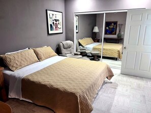 Ein Schlafzimmer mit Bett, Stuhl, Schreibtisch und einer Tür zu einem weiteren Raum.