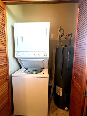 A compact laundry room with a front-loading washer and dryer, a water heater, and a hose. - Puerto Viejo C-3 | Waterfront 3BR on the Malecón (Puerto Peñasco)