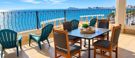 En terrasse med bord og stole, havudsigt og gelænder.