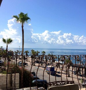 A balcony with a view of the ocean, palm trees, and a parking area with cars. - Puerto Viejo B-2 | Oceanview 3BR on the Malecón (Puerto Peñasco)