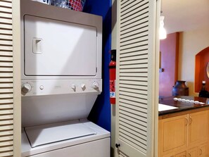 A laundry room with a washing machine and dryer, a fire extinguisher, and a countertop with various items. - Puerto Viejo B-2 | Oceanview 3BR on the Malecón (Puerto Peñasco)