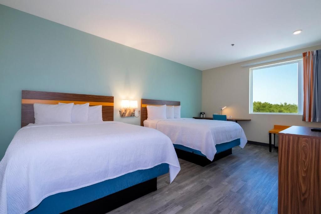 A hotel room with two beds, a desk, and a window with curtains.