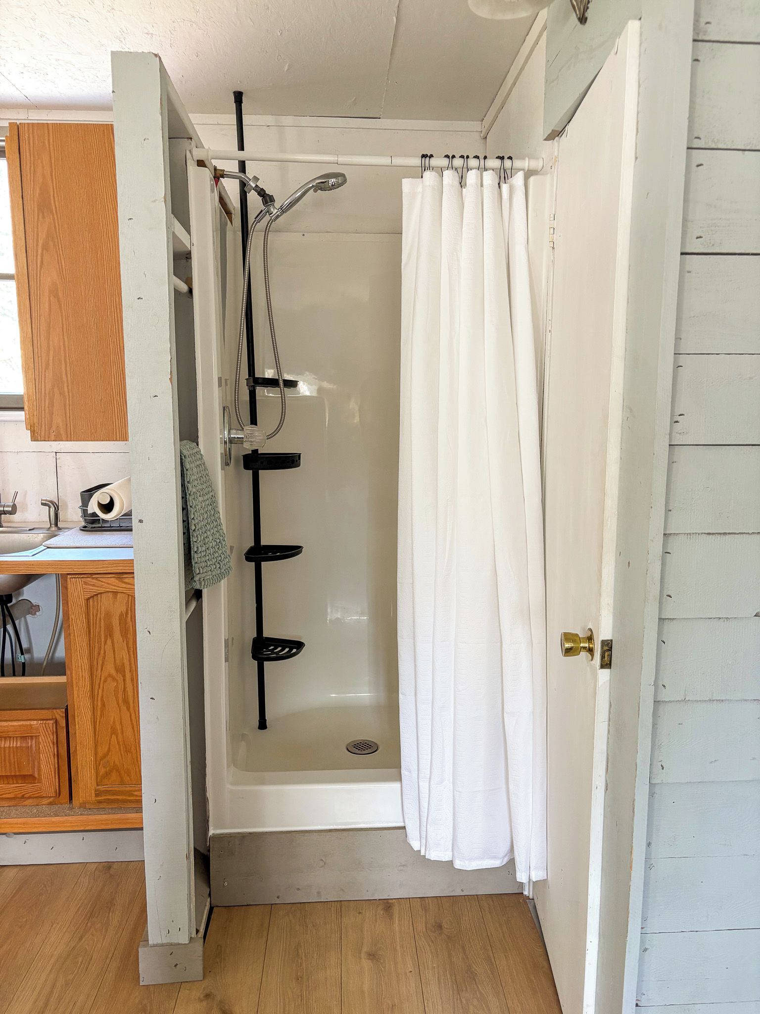 A shower area with a white curtain, a handheld showerhead, and a black hose.