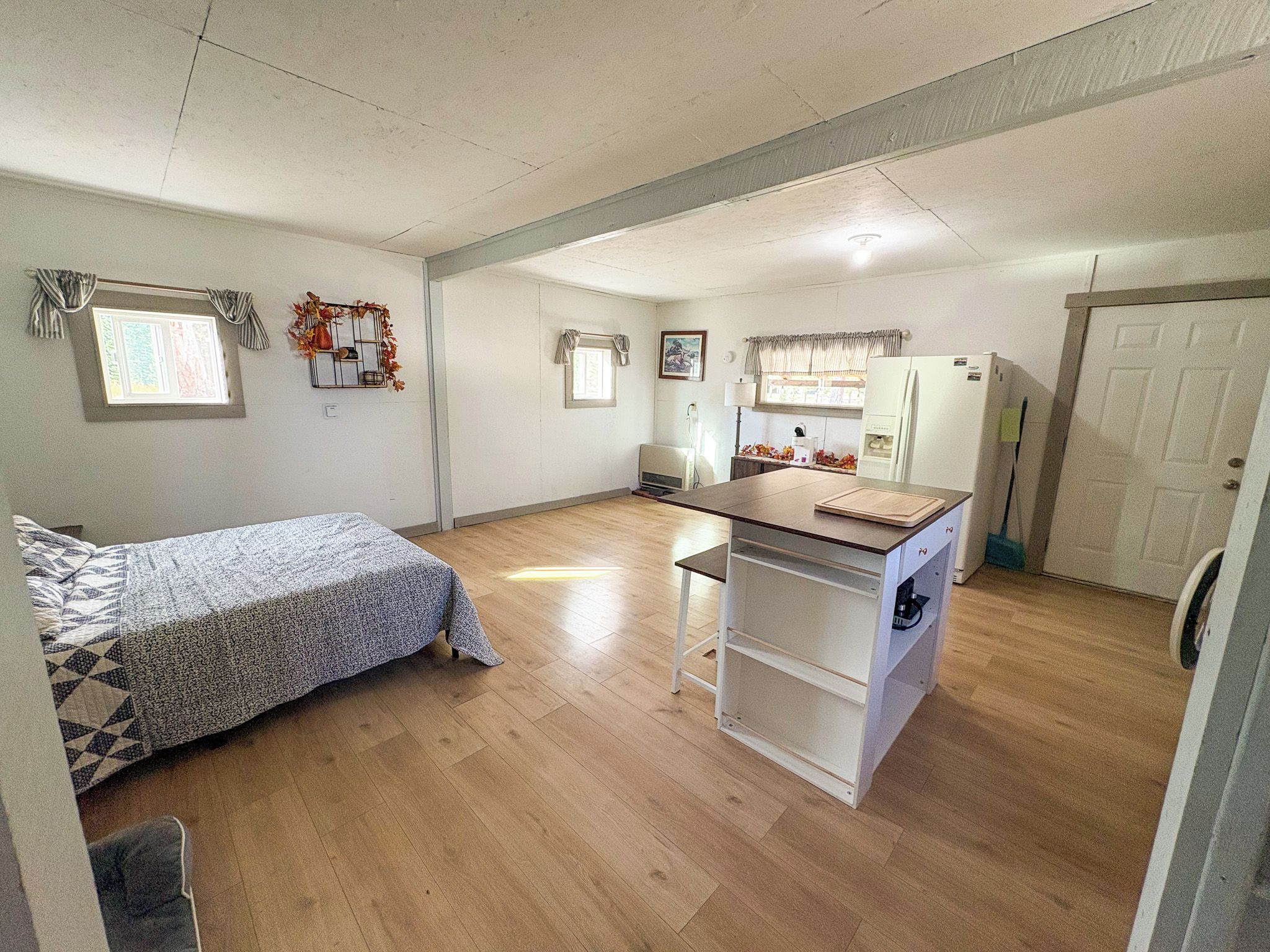 Una cocina compacta con refrigerador, una pequeña mesa de comedor y una ventana con cortinas.