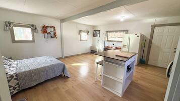Una cocina compacta con refrigerador, una pequeña mesa de comedor y una ventana con cortinas.