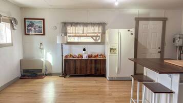 A kitchen with a refrigerator, a wooden cabinet, a window with curtains, and a lamp.
