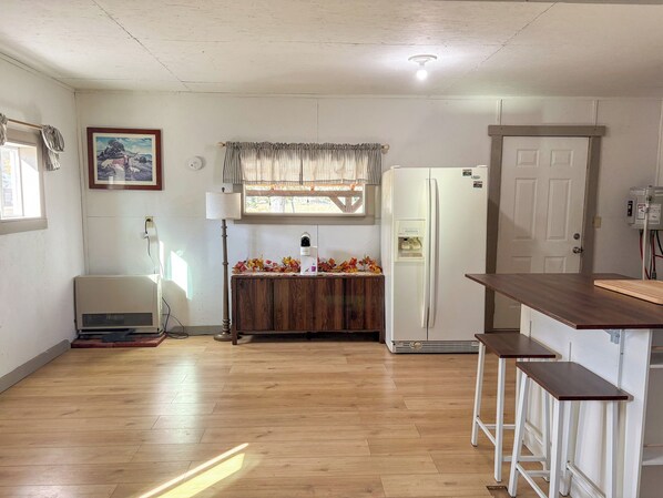 A kitchen with a refrigerator, a wooden cabinet, a window with curtains, and a lamp.