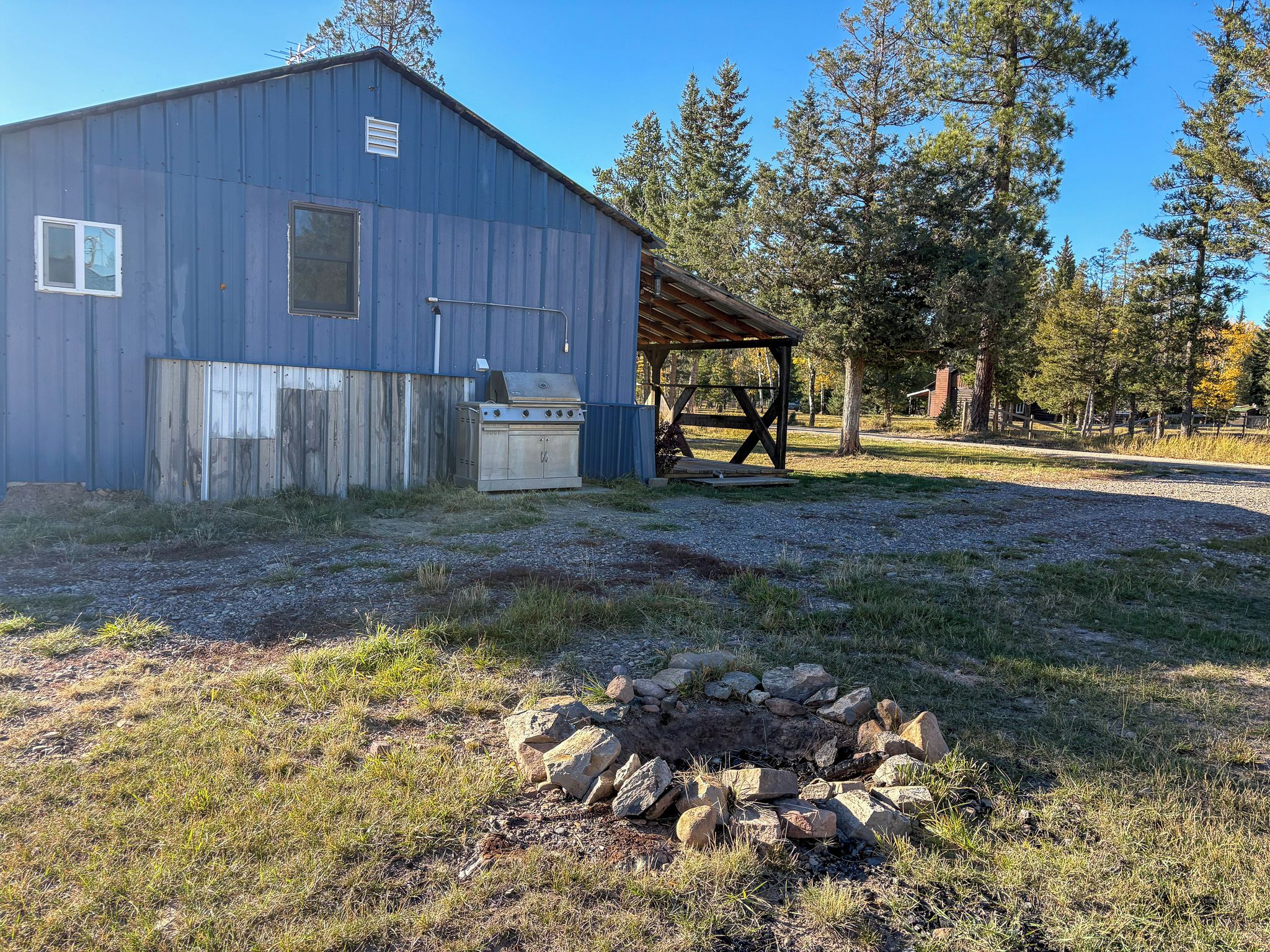 A rustic outdoor area with a metal building, a covered seating area, and a fire pit.