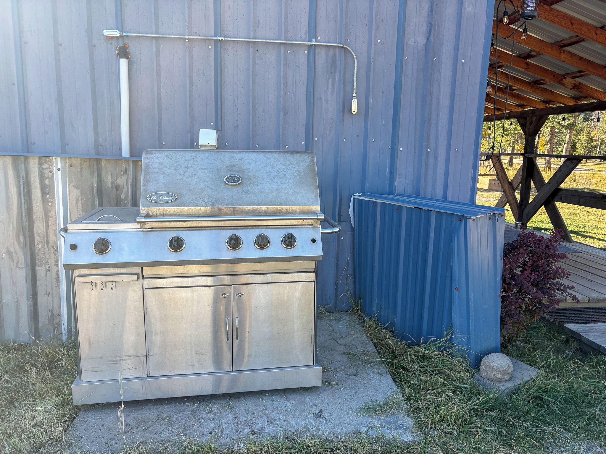 Una parrilla de gas portátil con un gabinete de metal y una chimenea, ubicada frente a un edificio azul de metal.