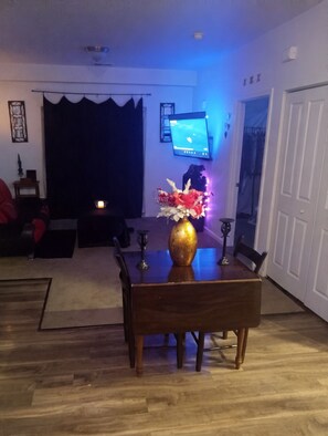 A dining area with a wooden table, chairs, a vase with flowers, a television mounted on the wall, and a door to the right. - Fabulous 1-bedroom apartment with AC in charming Lawrence (Lawrence)