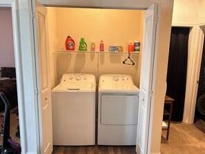 A laundry room with two front-loading washing machines and a shelf above containing various cleaning products. - Fabulous 1-bedroom apartment with AC in charming Lawrence (Lawrence)