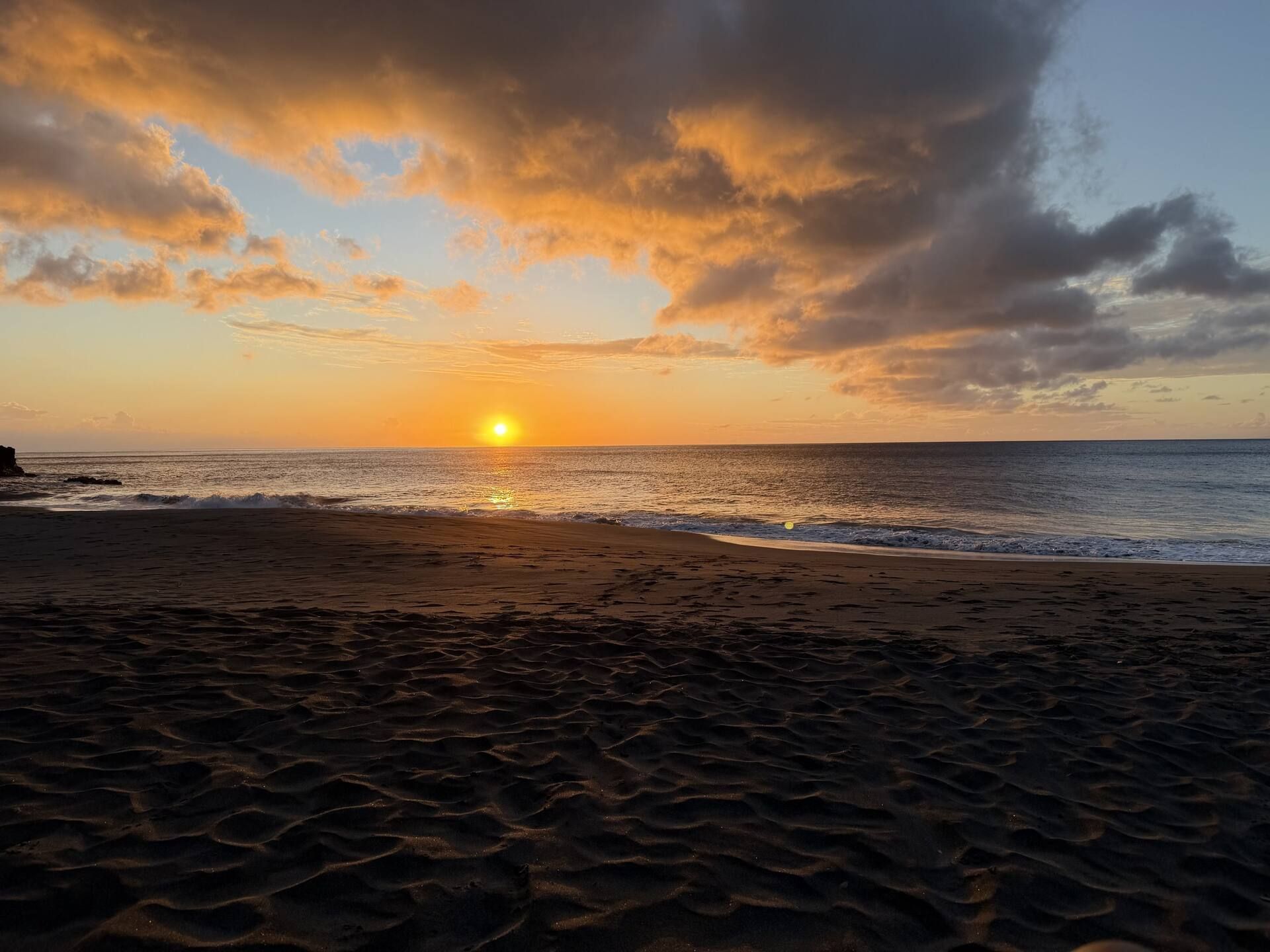 Uma praia com um pôr do sol, ondas e céu claro.