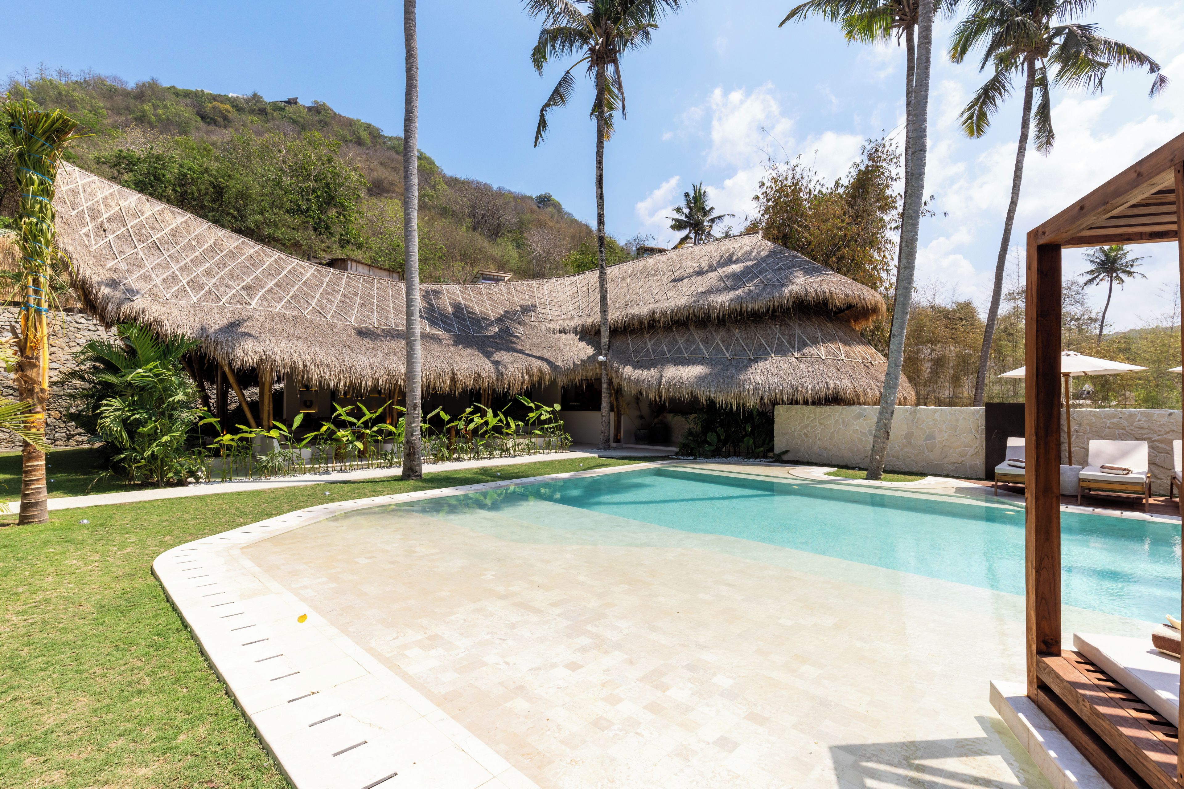 A swimming pool with a thatched-roof structure and lounge chairs in the background.
