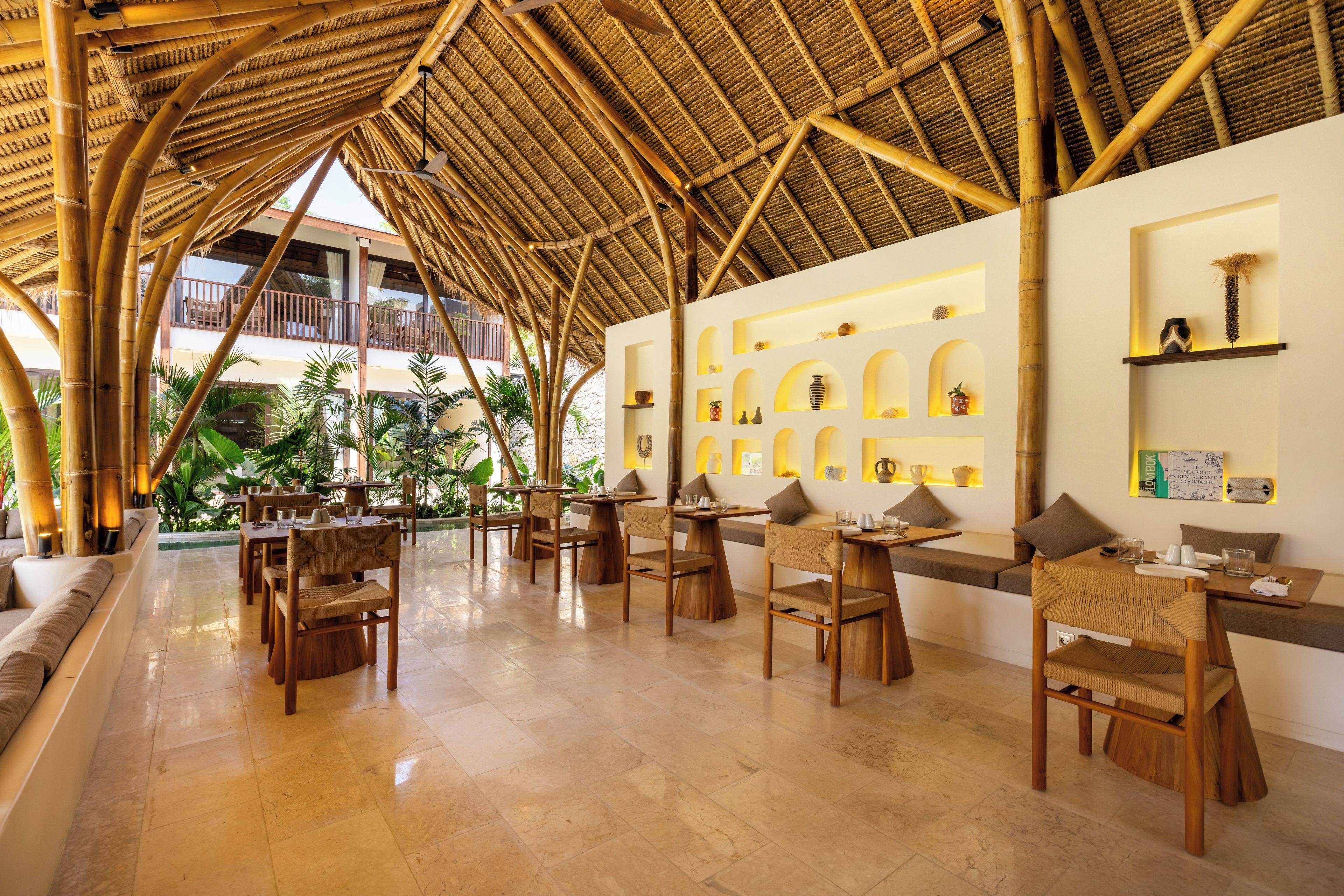 Restaurante com teto de bambu, mobiliário de madeira e vista para o exterior.