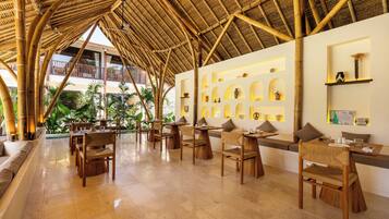 Restaurante com teto de bambu, mobiliário de madeira e vista para o exterior.