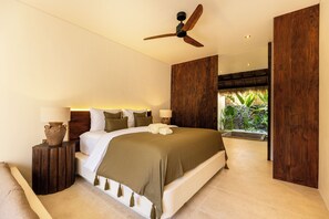A modern bedroom with a large bed, a ceiling fan, and a view of a tropical garden.