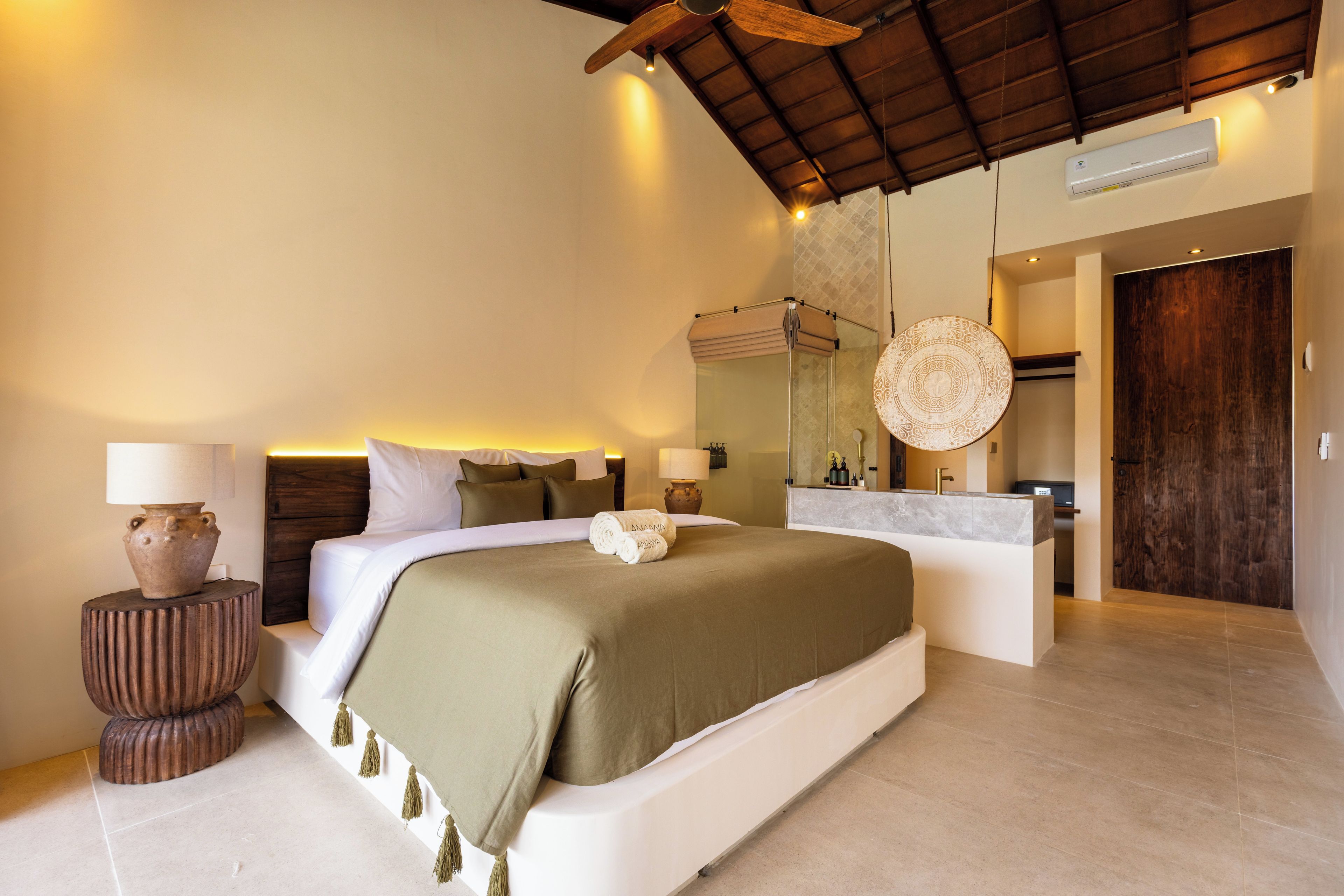 Ein modernes Hotelzimmer mit einem großen Bett, einem Badezimmer mit Waschtisch und einem Deckenventilator.