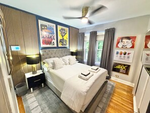 A modern bedroom with a tufted headboard, a bed with white linens, a standing lamp, and a ceiling fan.
