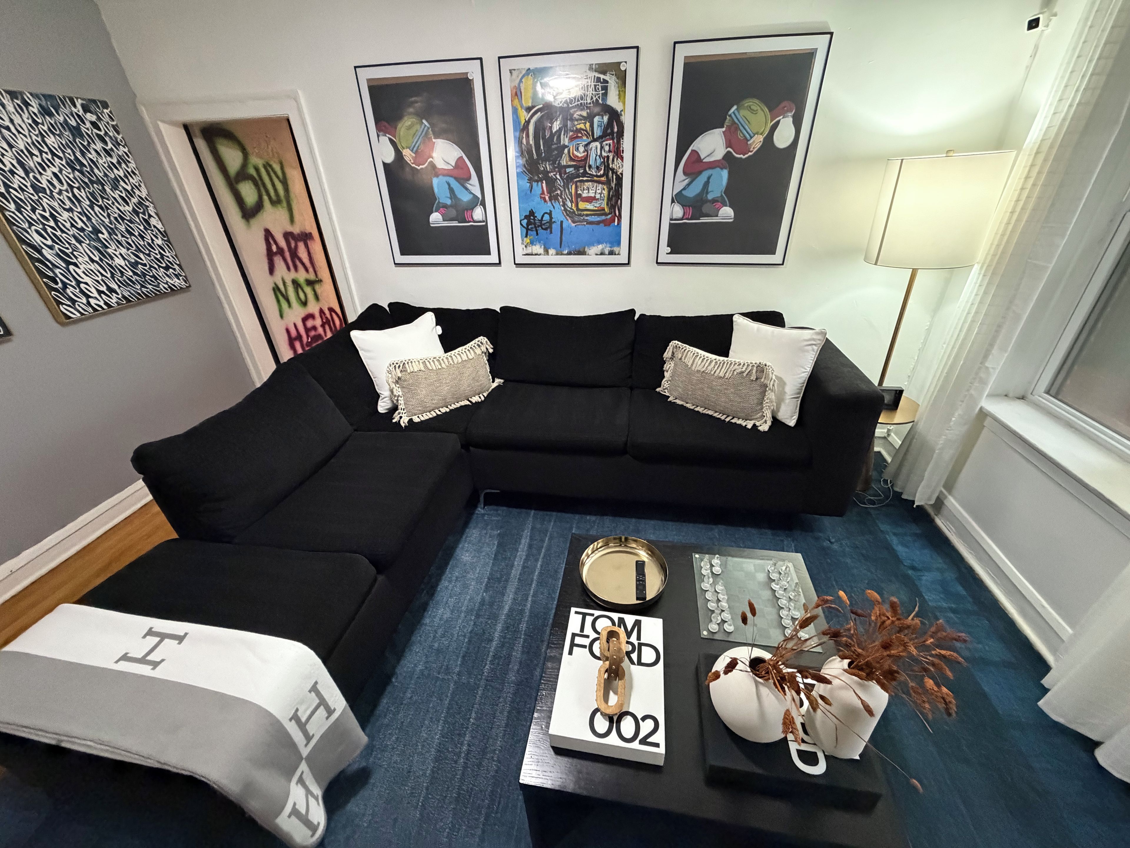 A living room with a sectional sofa, a coffee table with decorative items, and three framed artworks on the wall.