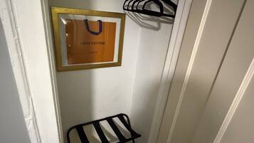 A narrow hallway with a framed Louis Vuitton bag on the wall, a black metal chair, and a black hanger rack.
