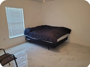 A bedroom with a bed, a chair, and a window with blinds. - Sun‑Soaked Living in the Heart of Florid, 3‑Bd House Available in Lehigh Acres! (Lehigh Acres)