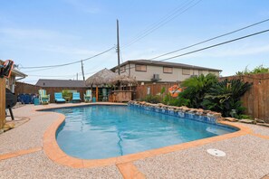A backyard with a swimming pool, a thatched-roof structure, and a wooden fence. - Escape to your private Poolside Paradise - Backyard Oasis w/pool & palapa.  Min (Galveston)