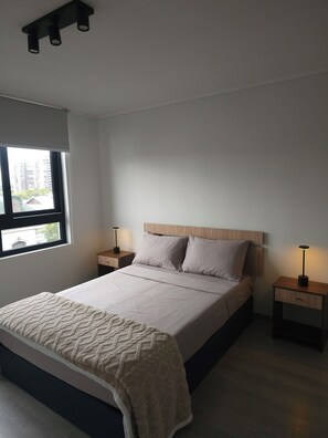 Une chambre à coucher comprenant un lit, deux tables de chevet, une fenêtre et un luminaire au plafond.