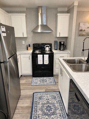A modern kitchen with stainless steel appliances, white cabinetry, and a central stove. - Marie's Hideaway (Keystone Heights)