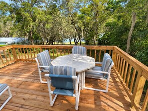 A wooden deck with a round table and four chairs, surrounded by a wooden railing. - Marie's Hideaway (Keystone Heights)