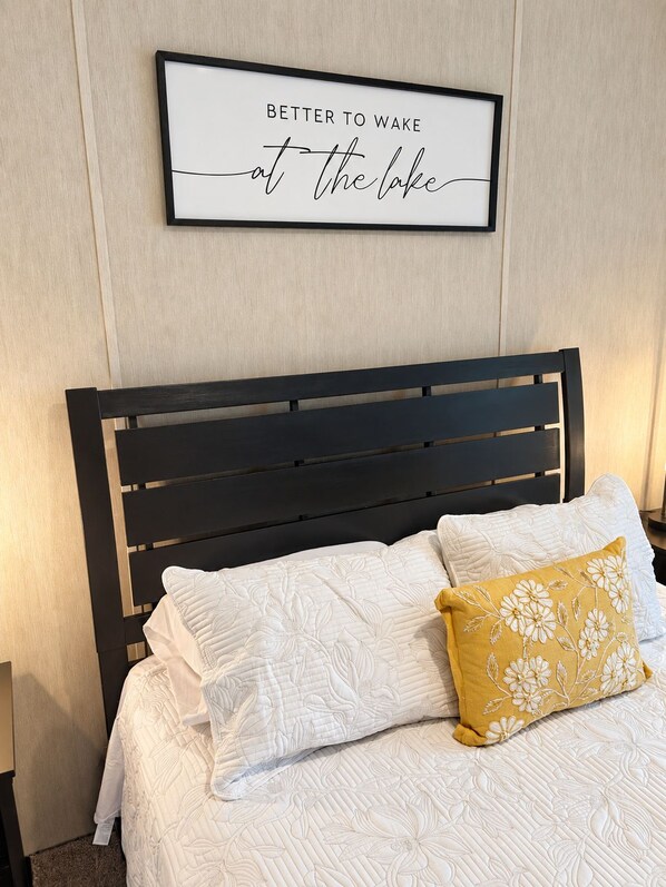 A neatly made bed with white bedding and a single decorative pillow, a black headboard, and a framed inspirational quote on the wall. - Marie's Hideaway (Keystone Heights)