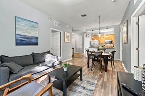 Ein modernes Wohnzimmer mit einem grauen Sofa, einem Couchtisch und einem Essbereich mit einem Holztisch und Stühlen.