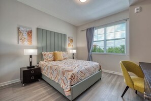 A bedroom with a bed, two bedside tables, a chair, and a window with curtains. - Stay Close to the Action, Spacious 3BR, Sleeps 8 (Orlando)