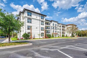 A multi-story hotel with a white facade, multiple balconies, and a parking lot in front. - Stay Close to the Action, Spacious 3BR, Sleeps 8 (Orlando)