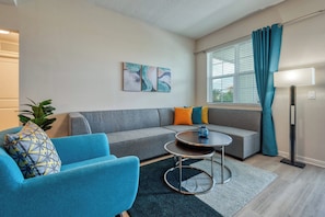 Un salon moderne avec un canapé gris, un fauteuil bleu, une table basse ronde et un lampadaire.