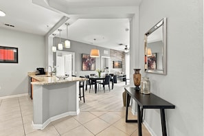 A modern kitchen with a central island, dining area with chairs, and a hallway leading to another room. - Orlando 3BR Condo, Space, Comfort and Location (Orlando)