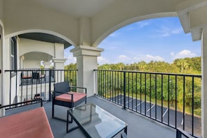 Ein Balkon mit Glastisch und Stühlen, Blick auf einen Parkplatz und ein Gebäude mit Bögen.