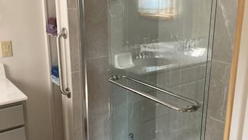 A glass-enclosed shower with a built-in bench, a towel rack, and a handheld showerhead.