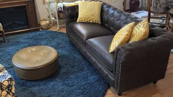 A living room with a leather sofa, round ottoman, and a television.
