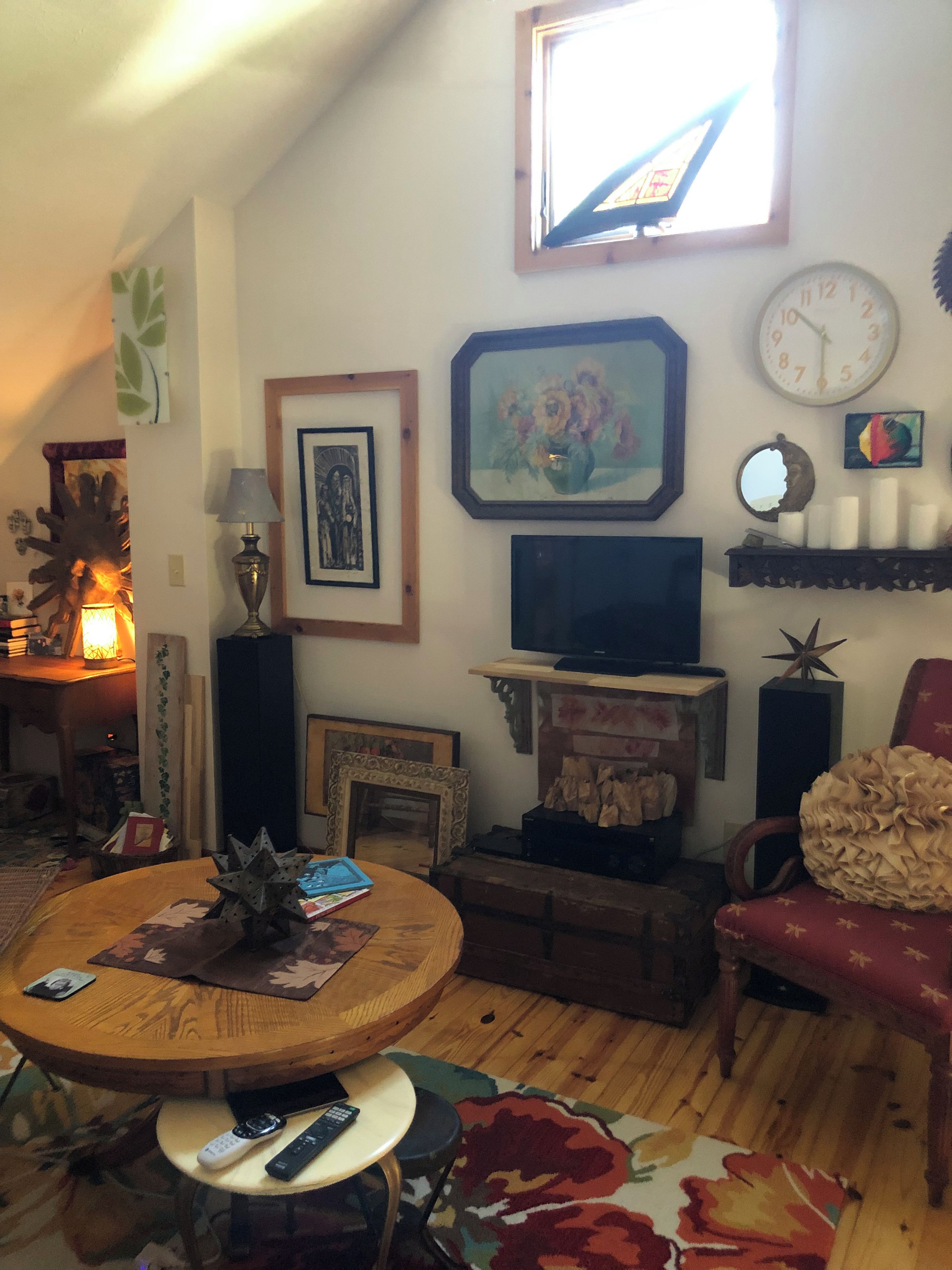 A cozy living room with a television, framed artwork, a clock, and a red armchair.