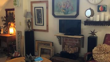 A cozy living room with a television, framed artwork, a clock, and a red armchair.