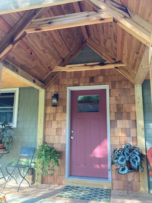 A wooden exterior with a red door, a small porch area, and potted plants.