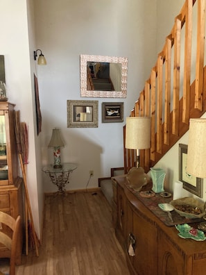 Una escalera de madera con barandilla, una mesita con lámpara y un espejo en la pared.