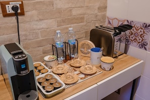 A kitchen counter with a coffee machine, water bottles, a toaster, and a tray of muffins. - Montefiori Luxury Suite (Bologna)