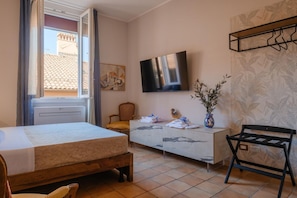 A hotel room with a bed, a TV, a desk, a chair, and a window with curtains. - Montefiori Luxury Suite (Bologna)