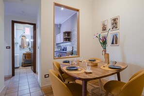 A dining area with a wooden table, yellow chairs, and a mirror reflecting the kitchen. - Montefiori Luxury Suite (Bologna)