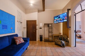 A living room with a blue sofa, a television mounted on the wall, and a patterned armchair. - Montefiori Luxury Suite (Bologna)