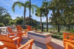Une terrasse extérieure avec des fauteuils Adirondack orange, un foyer et une vue sur un lac.
