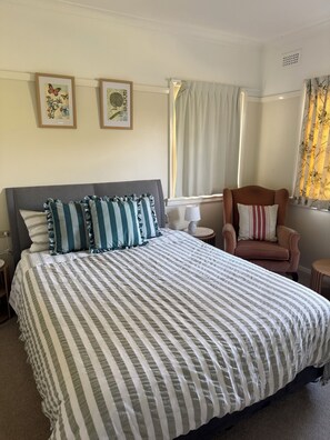 A hotel room with a bed, a chair, a lamp, and two framed pictures on the wall.