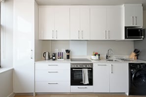 Une cuisine moderne avec des meubles blancs, un four à micro-ondes encastré, une bouilloire, un grille-pain et un lave-vaisselle.